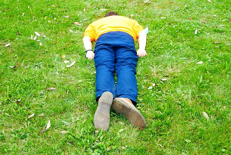 A body in orange sweatshirt and blue pants with brown boots lays with their face in a hole.