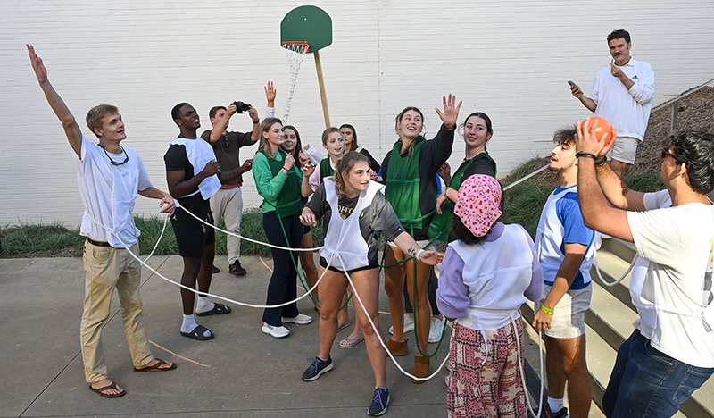 Players wearing green and white jerseys are bound by velcro connectors into teams. A basketball goal is mounted on a person.